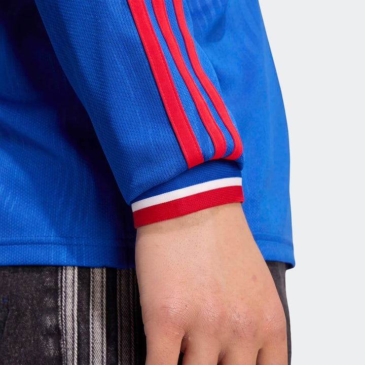 Close-up of a person's arm wearing a blue Manchester United 26/27 Away Longsleeve Jersey with red stripes and a red, white,