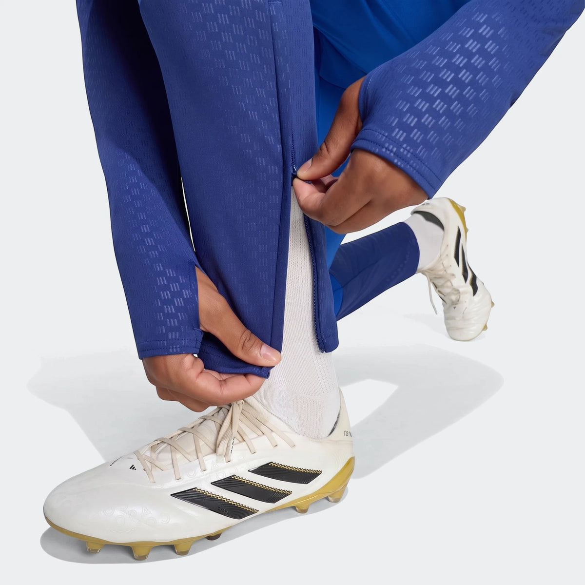 Close-up of a person zipping royal blue Manchester United 26/27 Cup Tiro Training Pants with textured fabric, shown with