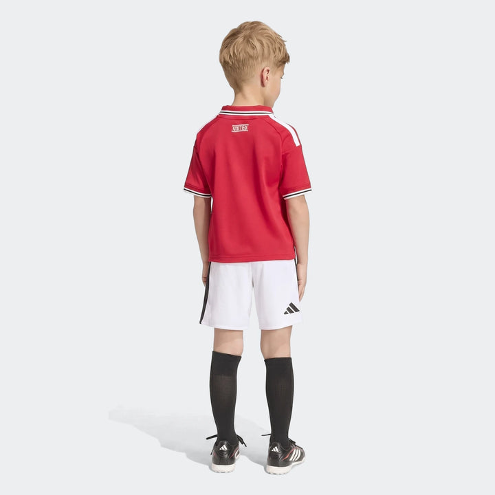 Child wearing Manchester United 26/27 Home Mini Kit, featuring a red jersey and white shorts, viewed from the back.