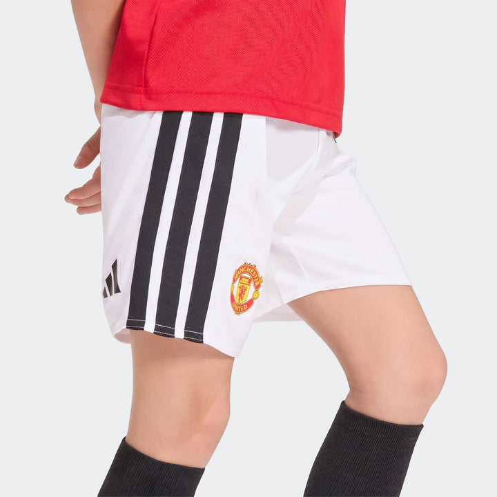 Close-up of a child wearing the Manchester United 26/27 Home Mini Kit, featuring a red jersey and white shorts with black