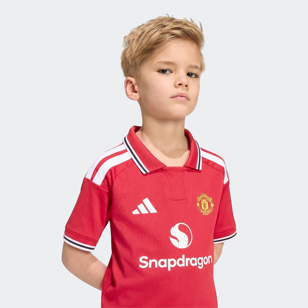 Front view of a child wearing the red Manchester United 26/27 Home Mini Kit jersey with club crest and sponsor logos.