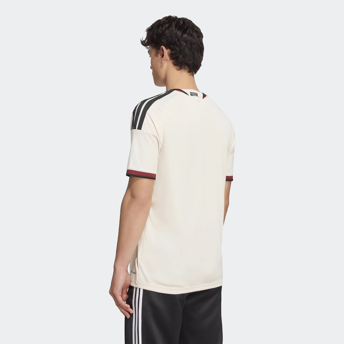 Male model wearing a cream Manchester United 26/27 Third Jersey with black stripes and shorts, rear view.