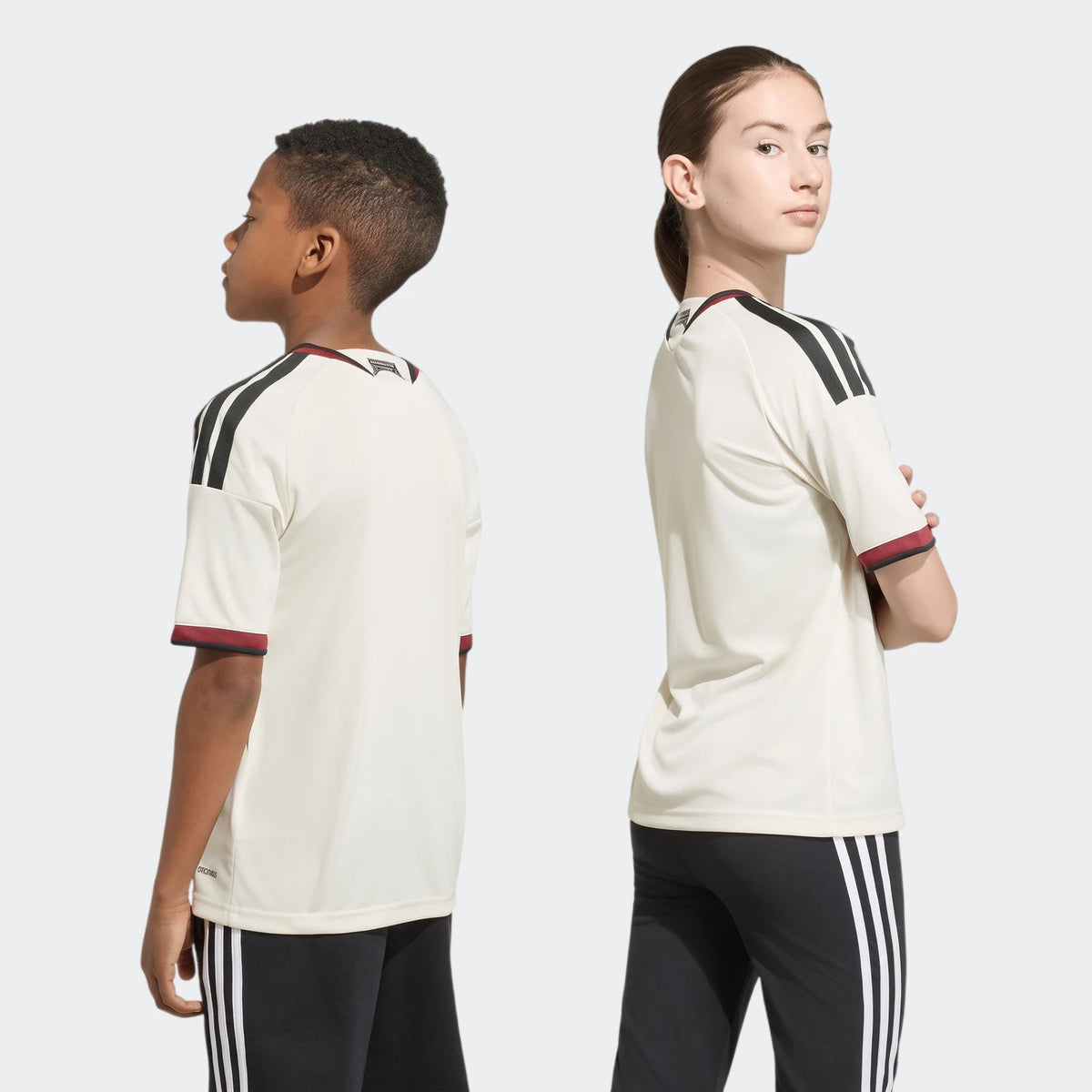 Cream Manchester United 26/27 Third Jersey Kids, featuring black shoulder stripes and red trim, worn by a boy and girl,