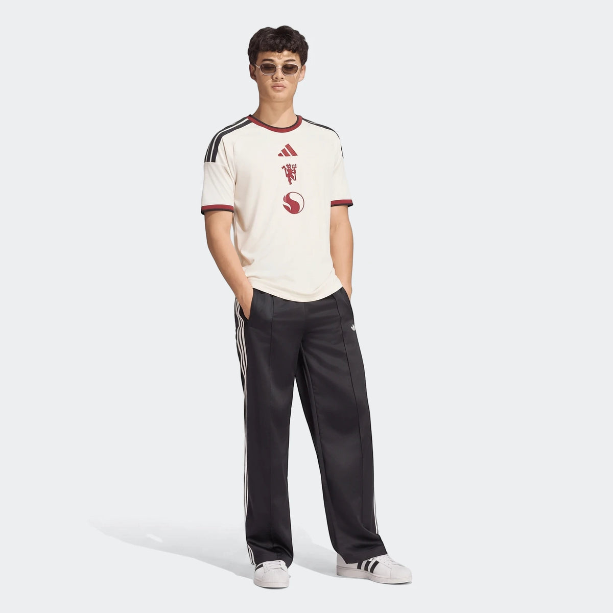 Male model wearing an off-white Manchester United 26/27 Third Jersey with black track pants, full-body view.