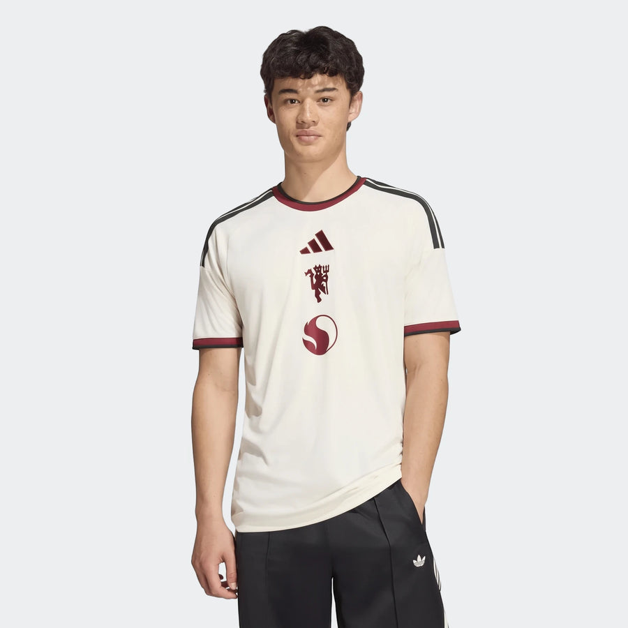 Male model wearing an off-white Manchester United 26/27 Third Jersey with dark red Adidas, devil, and S-shaped logos, and