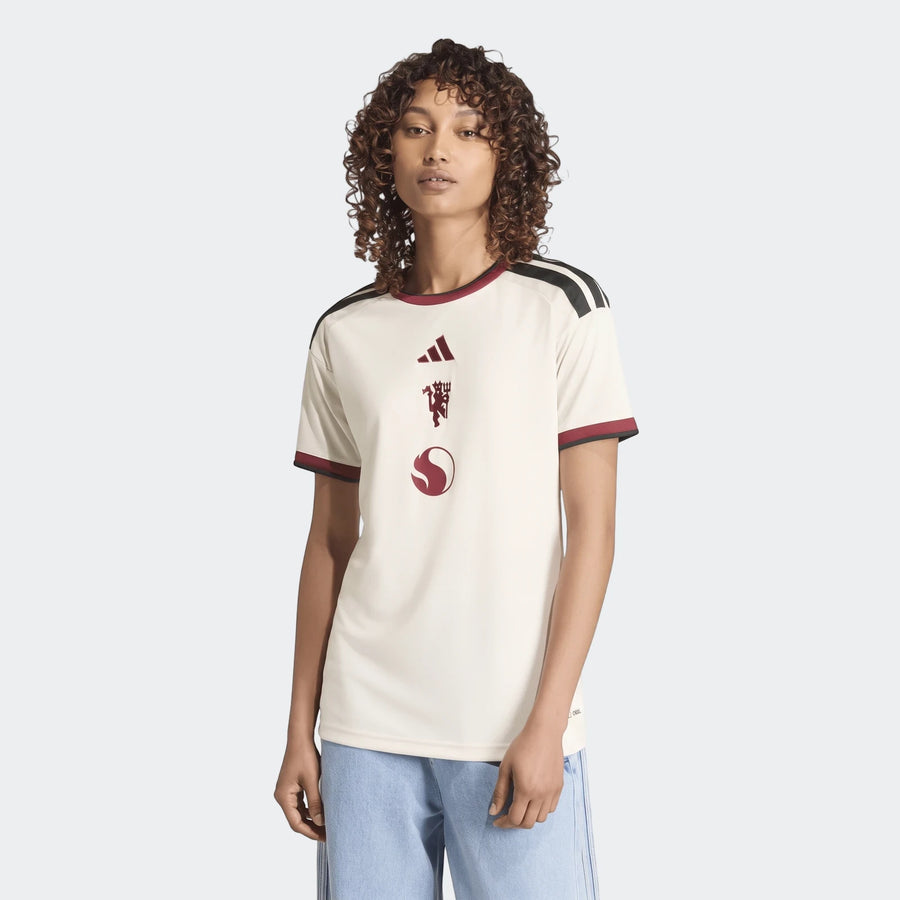 Woman wearing an off-white Manchester United 26/27 Third Jersey with maroon and black accents, short-sleeve.