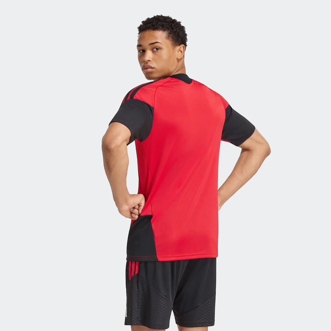Male model wearing a red and black Manchester United 26/27 Tiro Training Jersey, viewed from the back-right with hands on