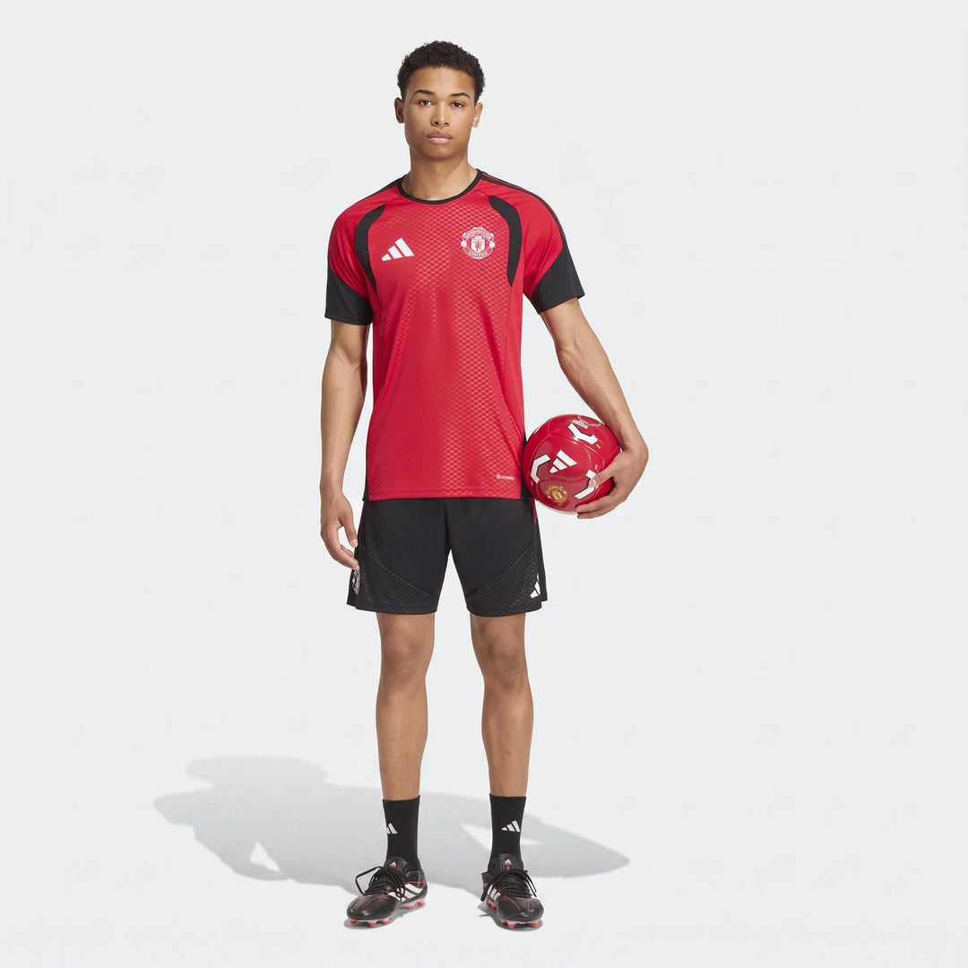 Male model wearing a red and black Manchester United 26/27 Tiro Training Jersey and black shorts, holding a soccer ball.