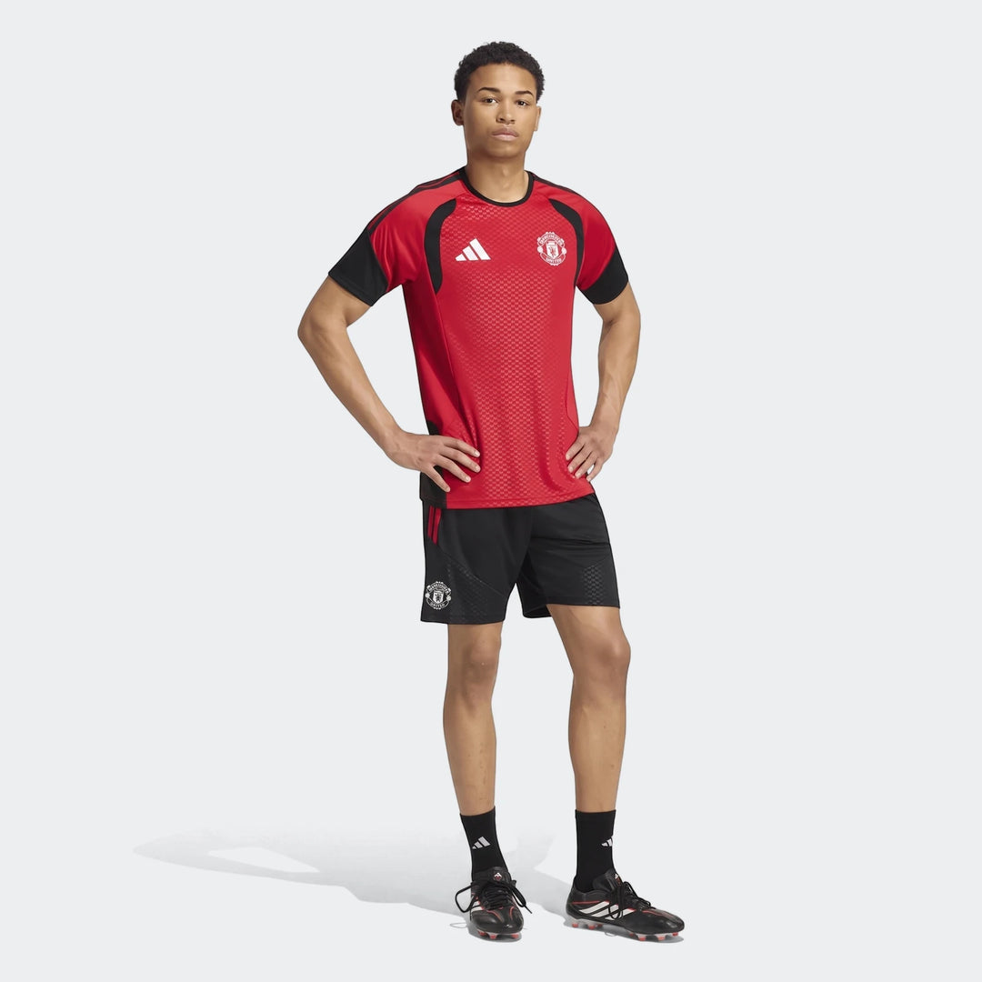 Male model wearing a red and black Manchester United 26/27 Tiro training jersey and black shorts, shown full body on white.