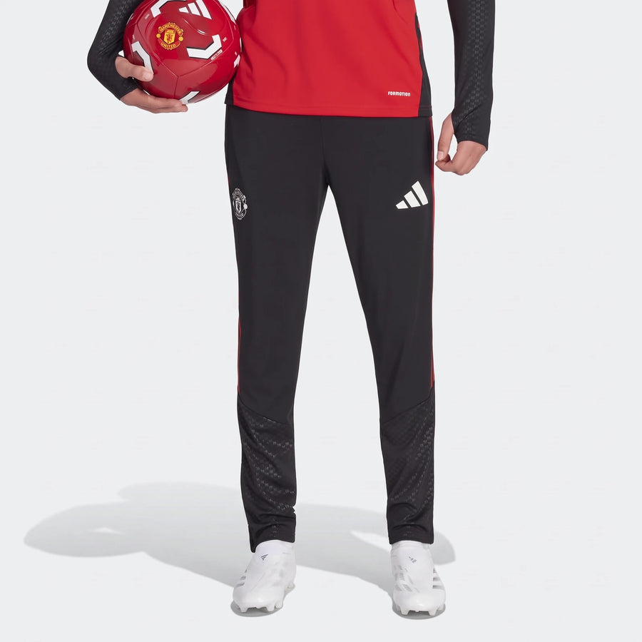 Black Adidas Manchester United 26/27 Tiro training pants with red stripes, worn by a player holding a soccer ball and white