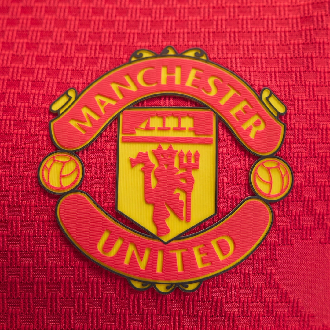 Manchester United 26/27 Authentic Home Jersey close-up of red textured fabric with yellow and red club crest badge.