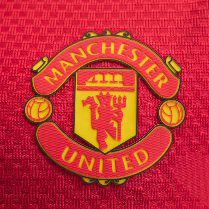 Manchester United 26/27 Authentic Home Jersey close-up of red textured fabric with yellow and red club crest badge.