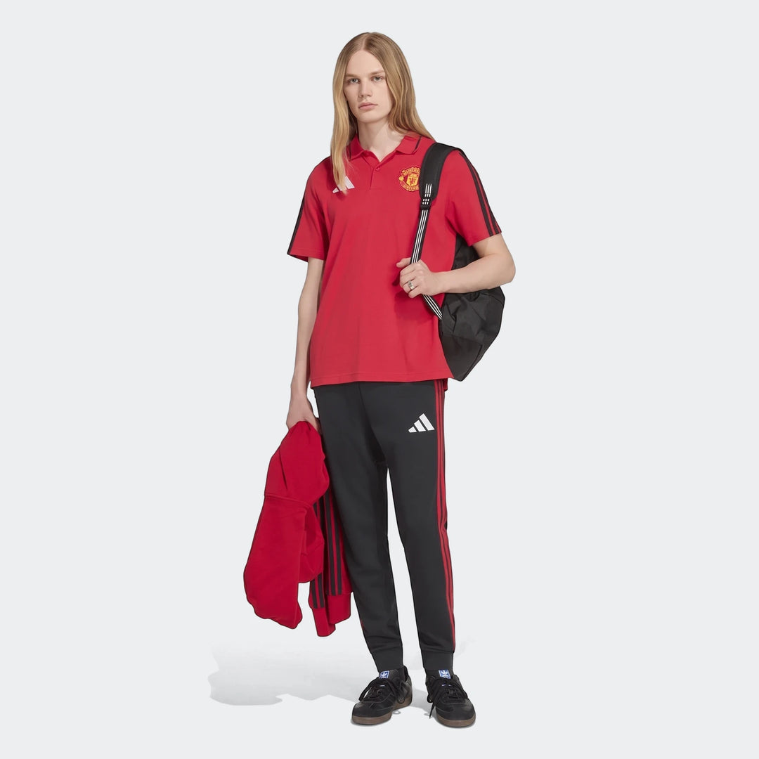 Red Manchester United DNA Polo Shirt worn by a model, paired with black track pants and a backpack, front view.