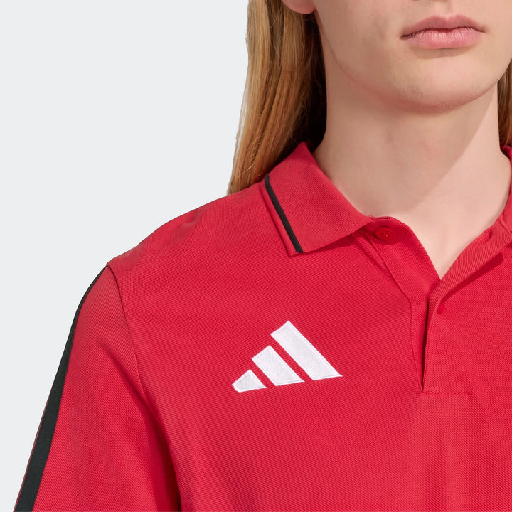 Close-up of a person wearing a red Adidas Manchester United Dna Polo Shirt, featuring a black collar stripe and white logo.