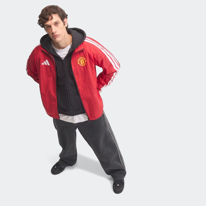Full-body shot of a male model in a red Adidas Manchester United Home Anthem Jacket, styled with dark gray jeans and black