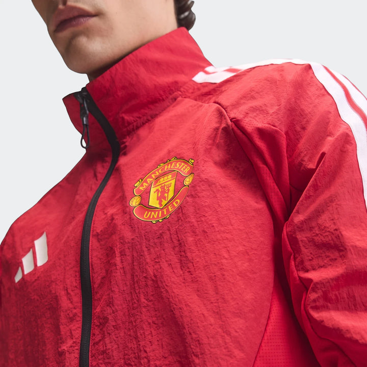 Close-up of a person wearing a red Manchester United Home Anthem Jacket with the club crest and white shoulder stripes.