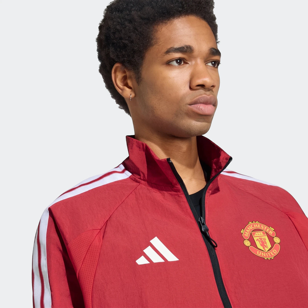 Close-up of a male model wearing a red Manchester United Home Anthem Jacket with white stripes and the team crest.