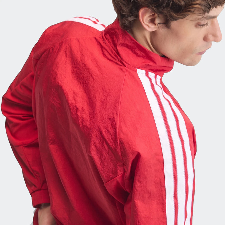 Red Manchester United Home Anthem Jacket with white stripes worn by a man in a side profile view, showcasing the athletic