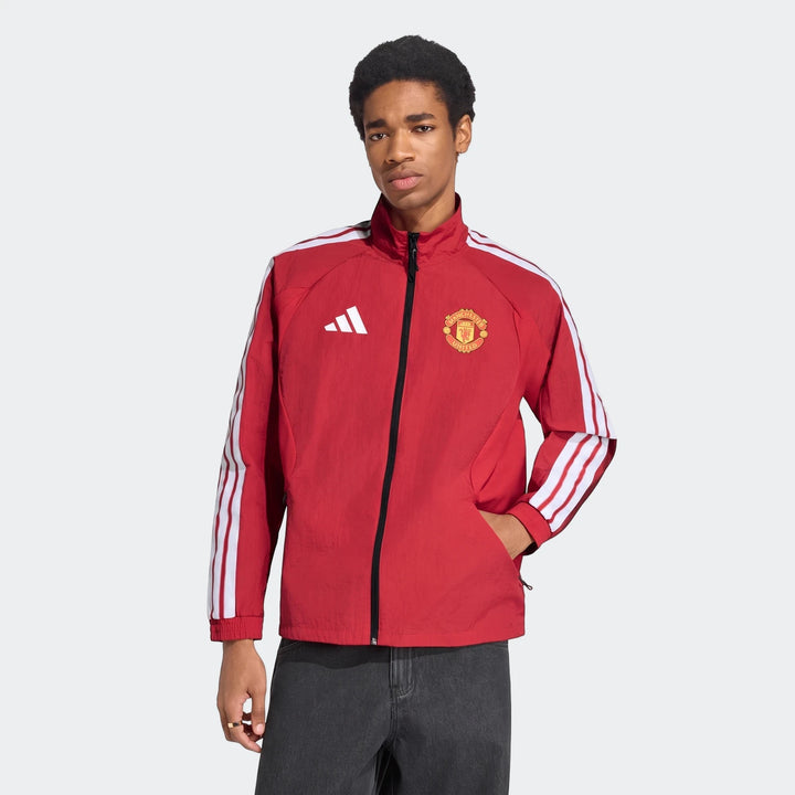 A man models the red Adidas Manchester United Home Anthem Jacket, featuring white three-stripes on the sleeves and the club