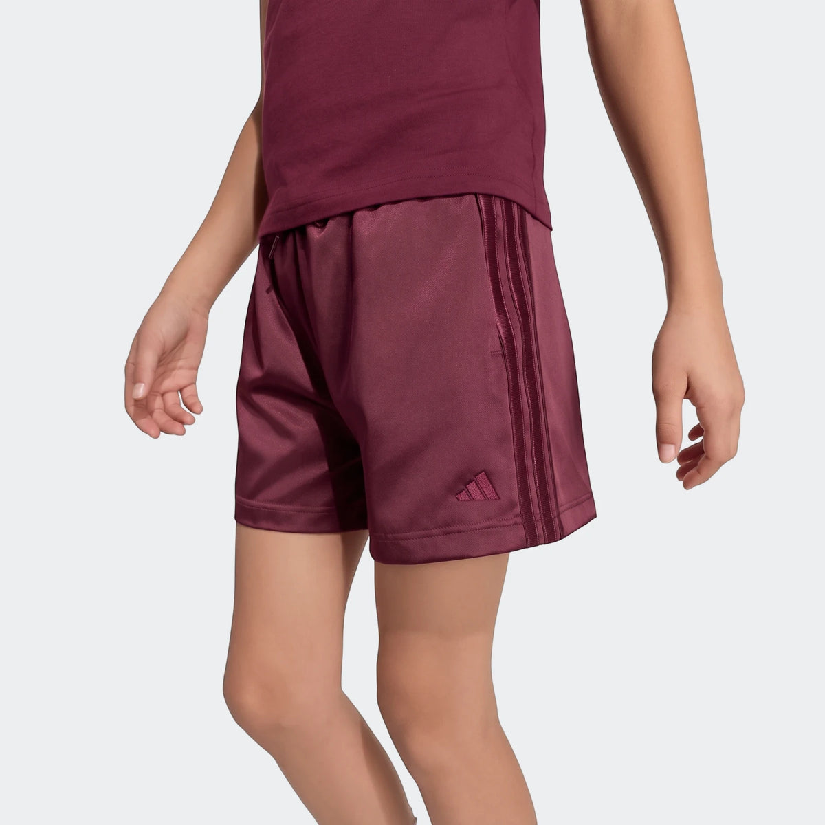 Maroon Adidas satin shorts for children, featuring three stripes on the side, modeled on a child.