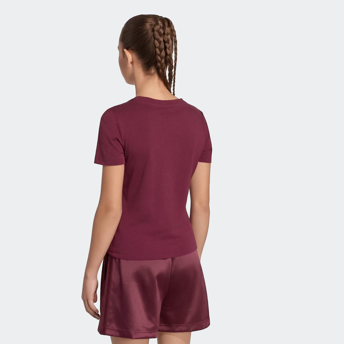 Young woman in a maroon satin t-shirt and matching shorts, viewed from the back.