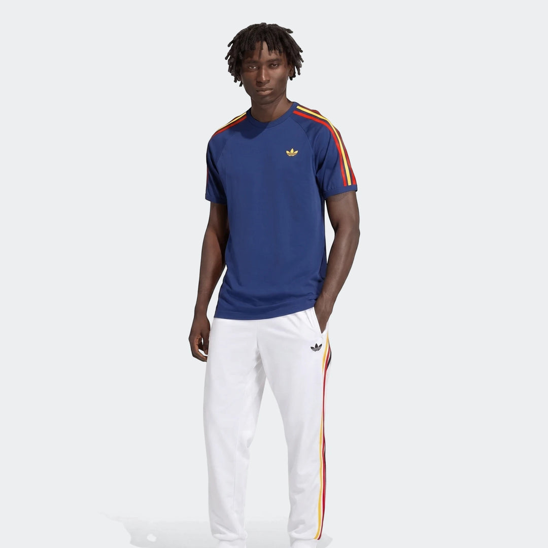 Male model wearing a navy blue Adidas 3-Stripes T-shirt with red and yellow raglan sleeve stripes and white track pants.