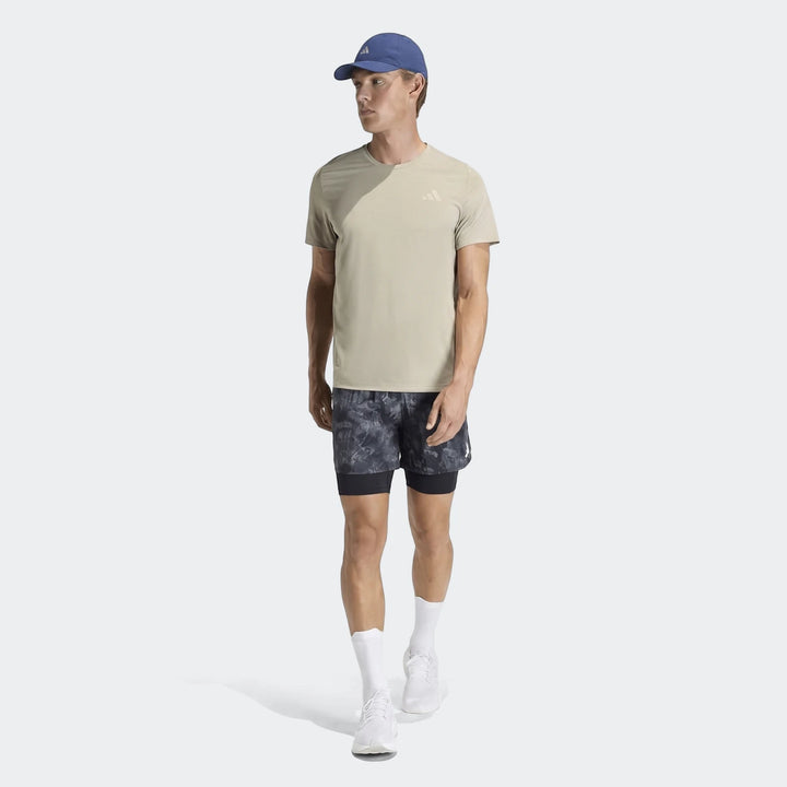 Men's Adidas Adi365 T-Shirt in khaki, paired with patterned shorts, blue cap, and white sneakers, full body view.