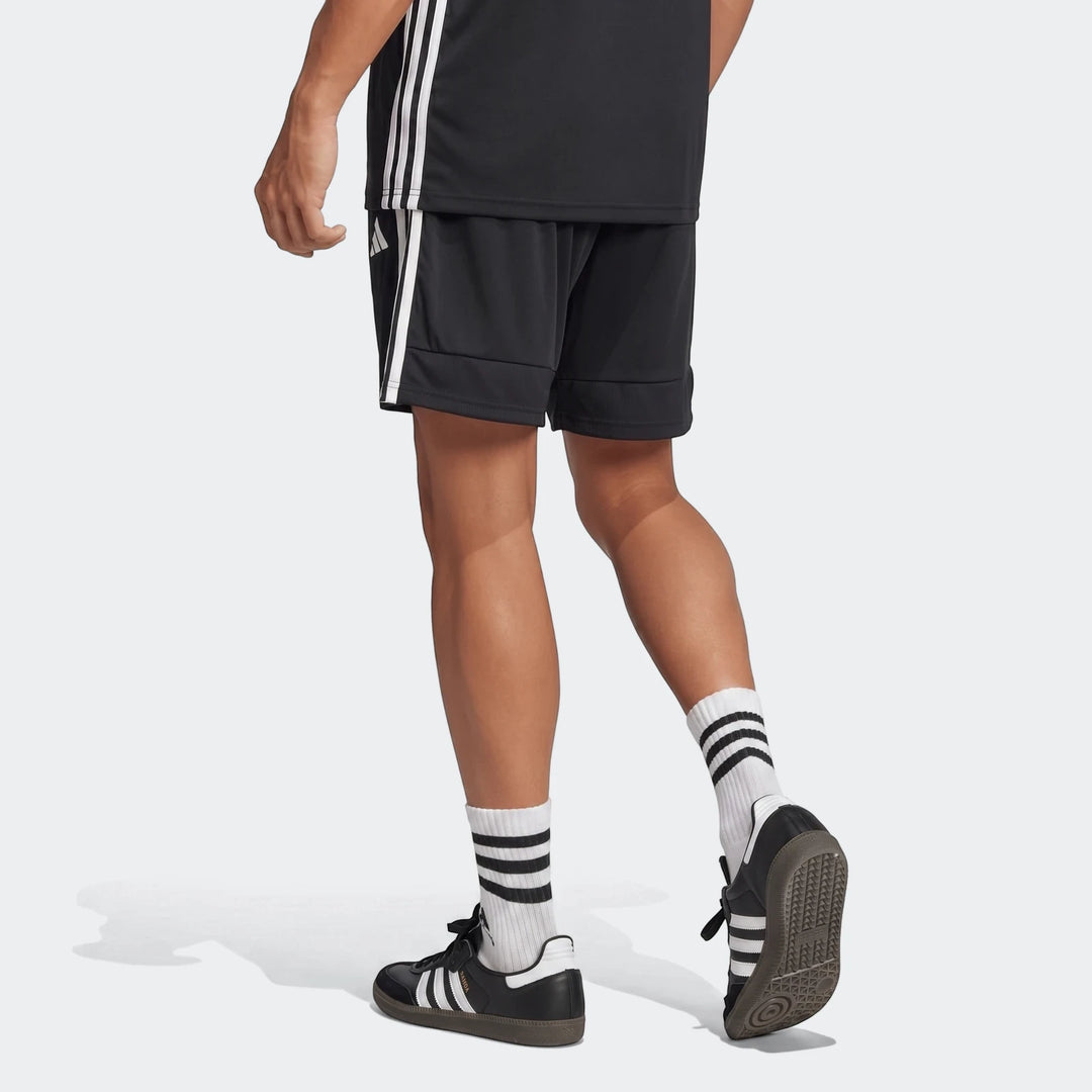 Men's black Adidas Tiro Essentials shorts with white three-stripes, worn from behind, paired with white striped socks and