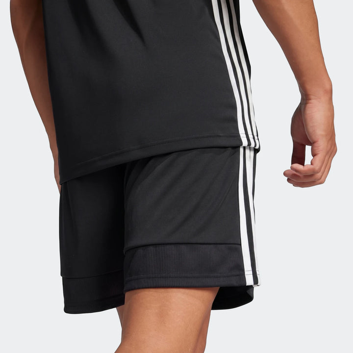 Men's black Adidas Tiro Essentials Shorts with white three-stripe detail on the side, modeled from a side-rear view.