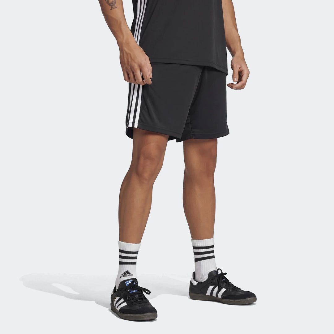 Men's black Adidas Tiro Essentials shorts with white three-stripe detailing, worn by a model in a partial body shot,