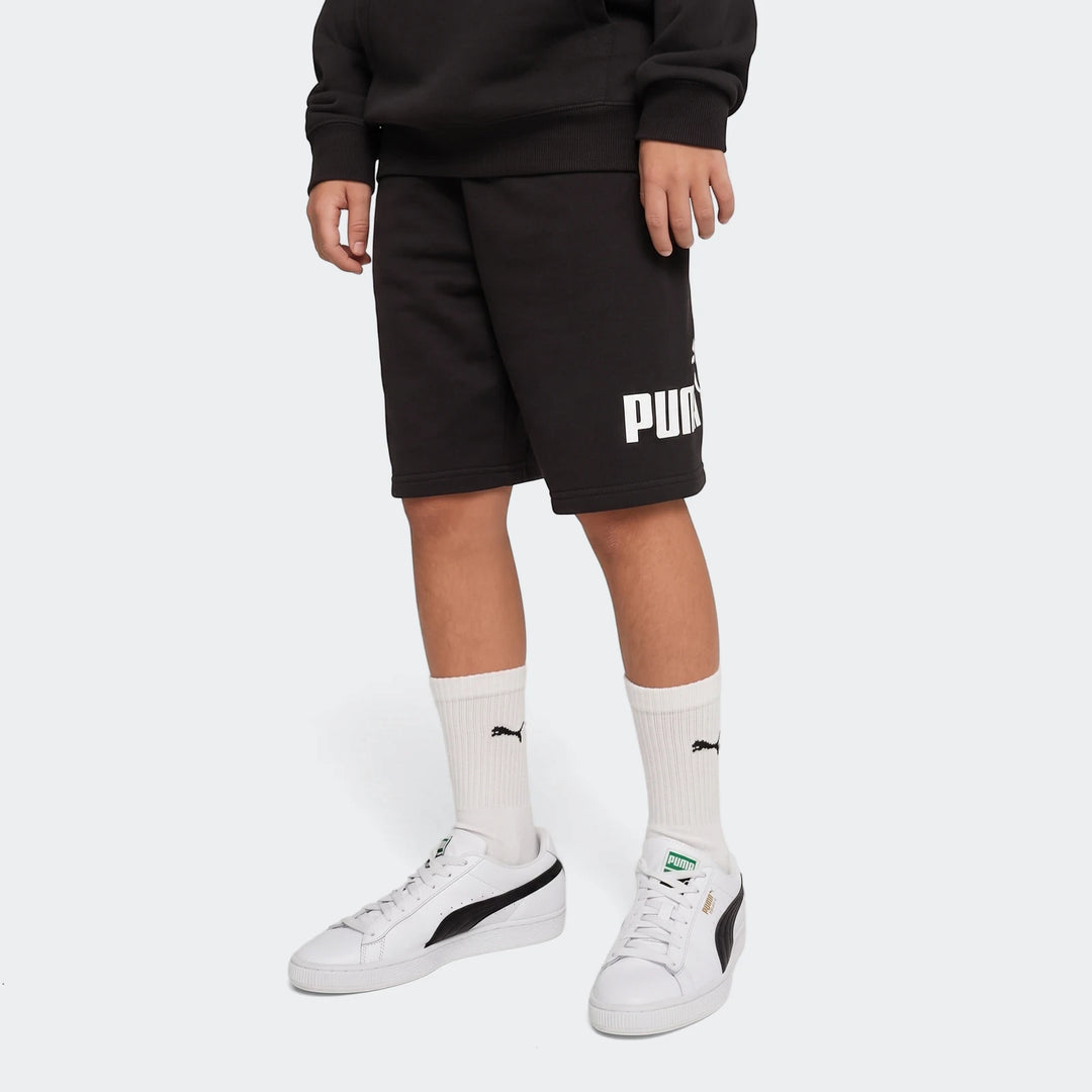 Men's black Puma Ess No. 1 Logo Shorts with white logo, featuring white socks and sneakers, worn by a model.
