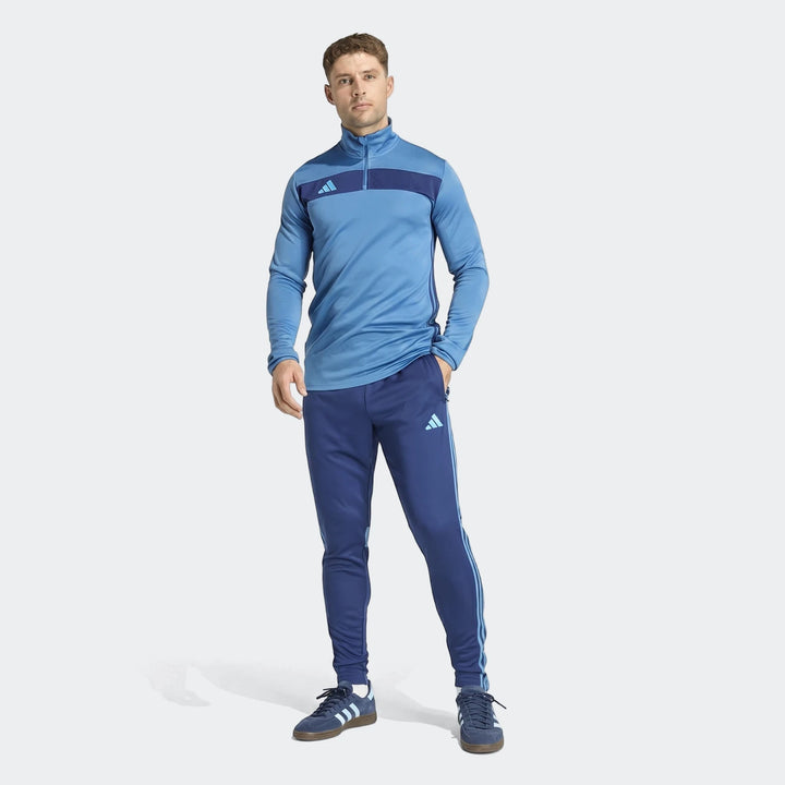 Male model wearing a blue Adidas Tiro Essentials Track Top and matching track pants, with dark blue Adidas sneakers, full