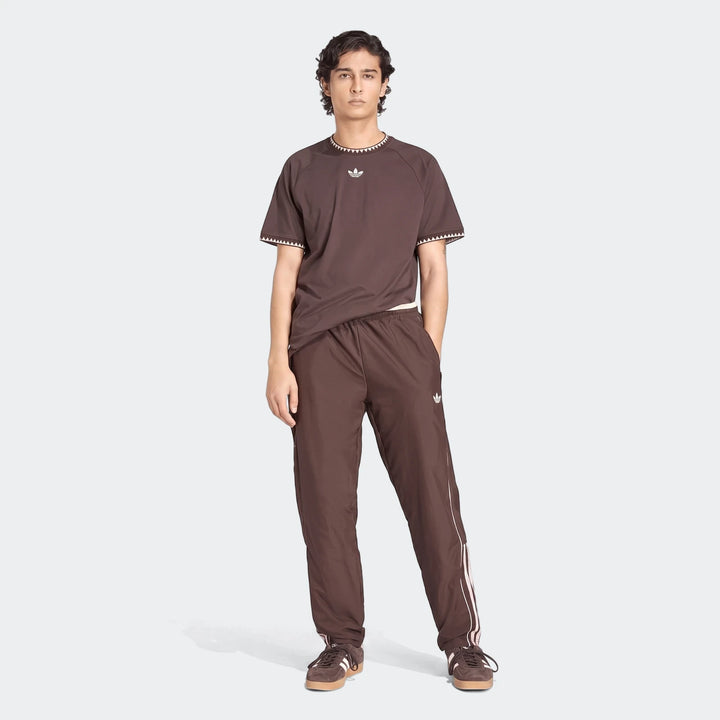 Male model wears a brown Chest Stripe Short Sleeve T-Shirt paired with track pants and sneakers.