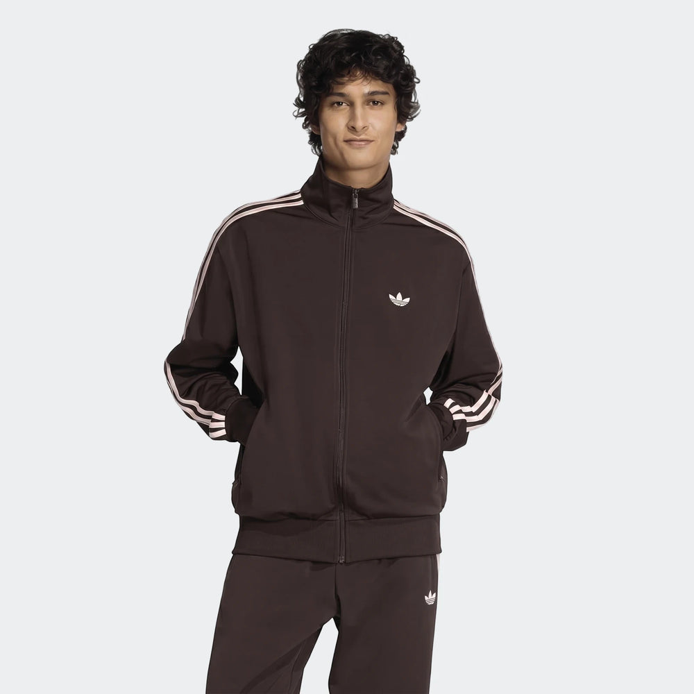 Men's dark brown Adidas Firebird Track Top and matching track pants, featuring white stripes and trefoil logos, worn by a