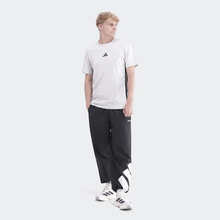 Full body shot of a man wearing a light grey 3-Stripes Single Jersey T-Shirt, black casual pants with white stripes, and