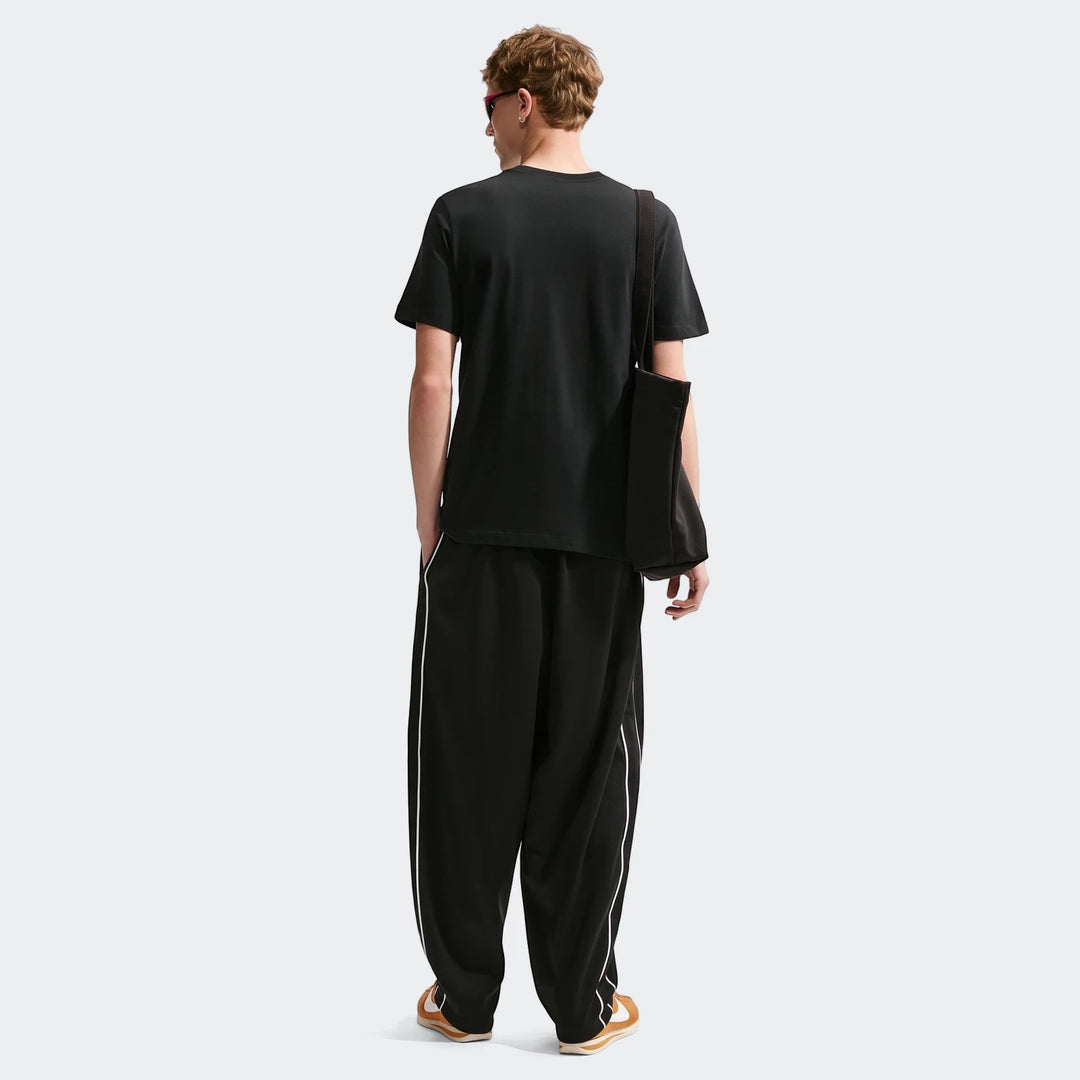 Men's Nike Sportswear black short-sleeve t-shirt shown from the back, paired with black track pants and sneakers.