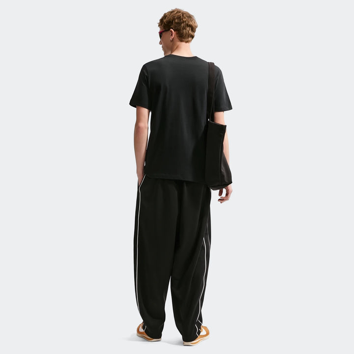 Men's Nike Sportswear black short-sleeve t-shirt shown from the back, paired with black track pants and sneakers.