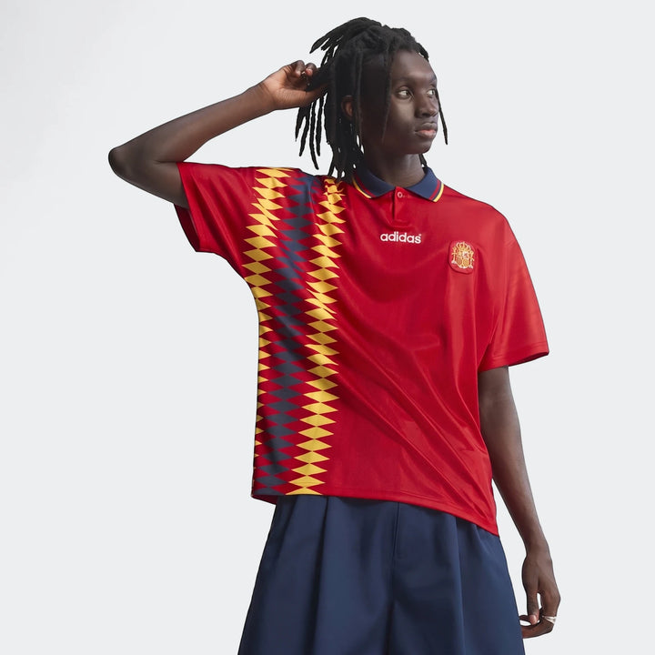 Young man in a red men's football jersey with navy collar and geometric pattern, paired with navy shorts, captured from