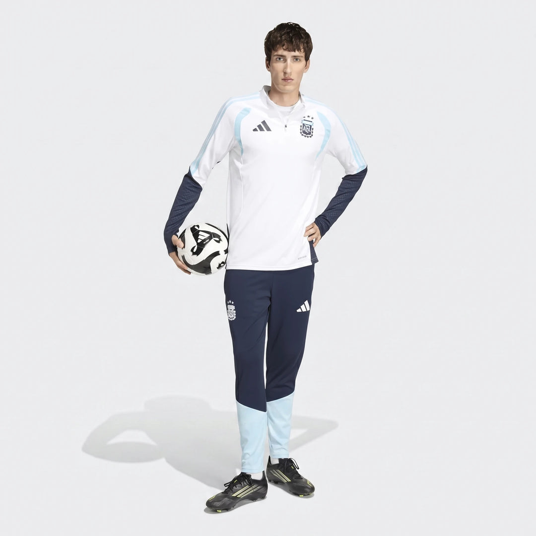 Male model wearing a white Adidas Argentina Training Top with matching dark blue pants and cleats, holding a soccer ball.