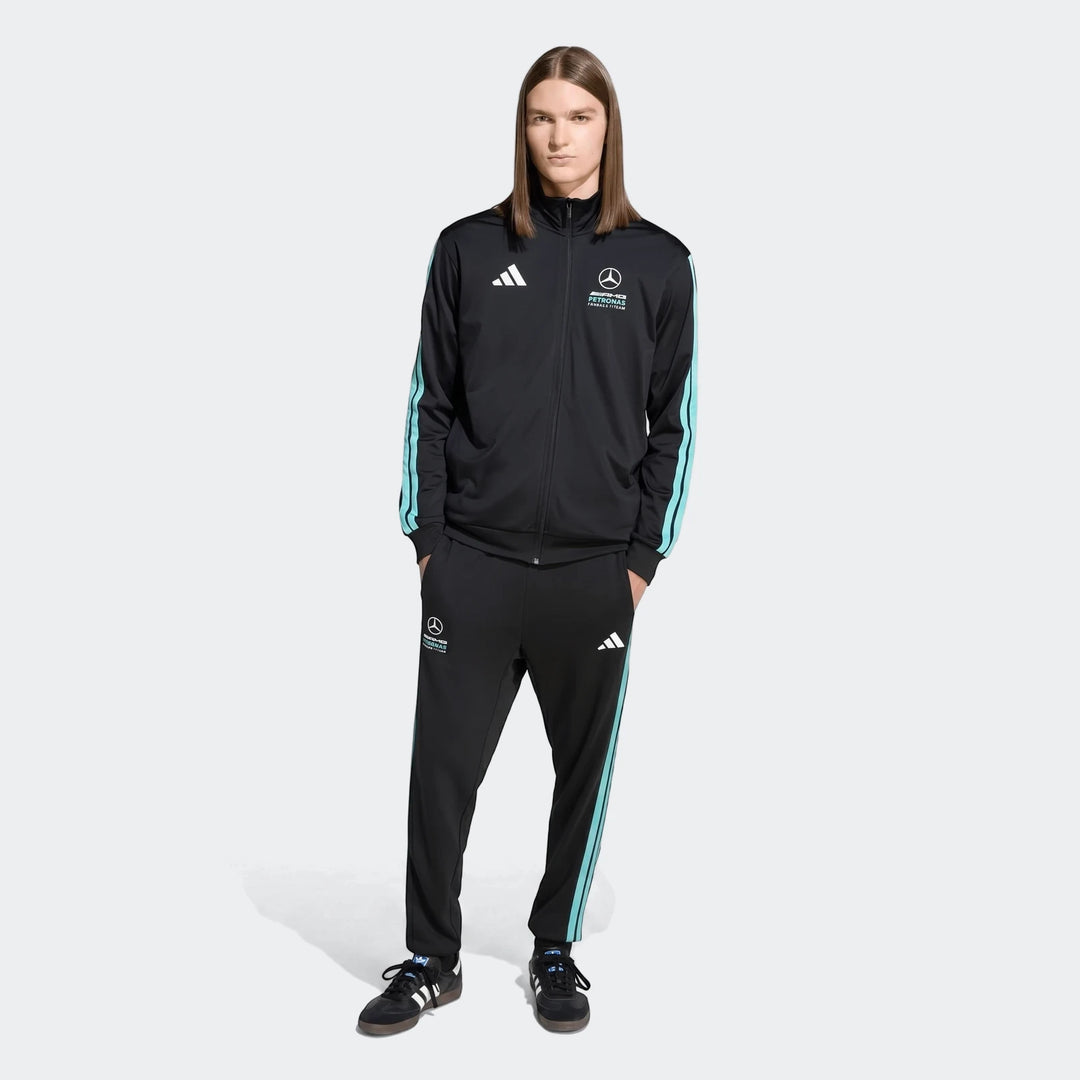 Male model wearing a black Mercedes-AMG Petronas Formula 1 Team DNA tracksuit with light blue stripes, full body view.