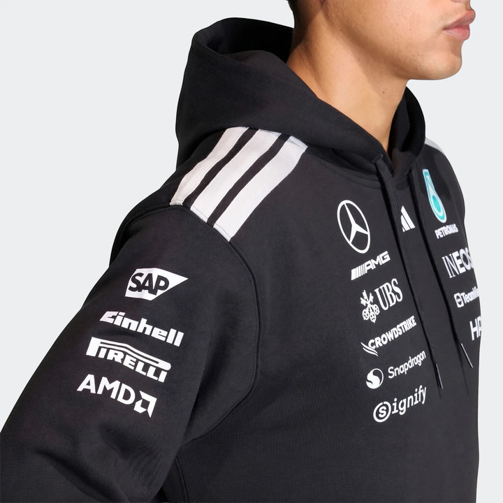 A model wears a black Mercedes-AMG Petronas Formula 1 Team Driver Hoodie featuring prominent sponsor logos on the chest and