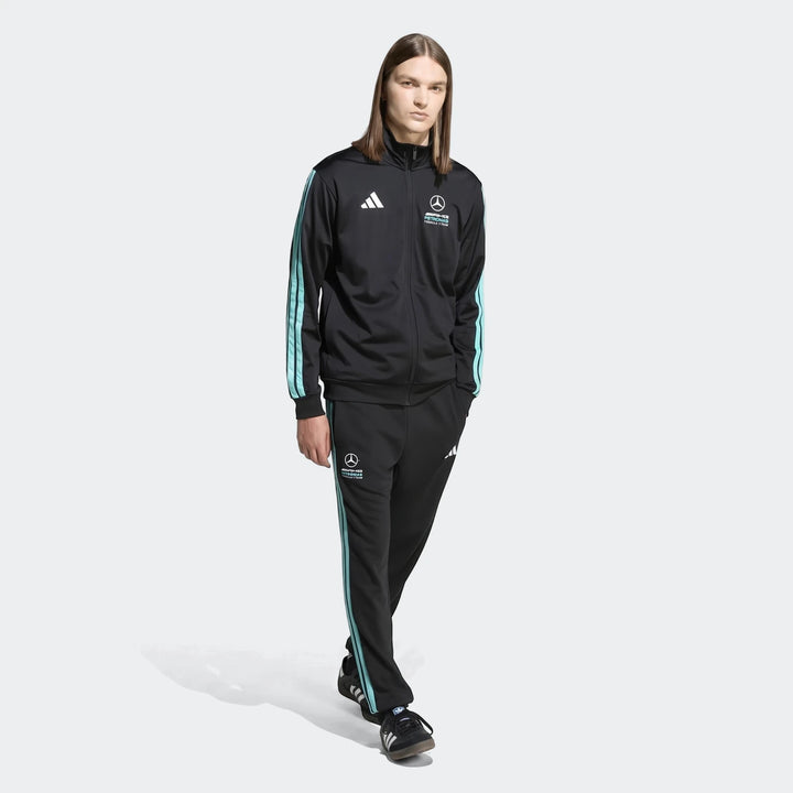 Full-body shot of a male model wearing a black Adidas Mercedes-AMG Petronas Formula 1 Team tracksuit with mint green stripes.