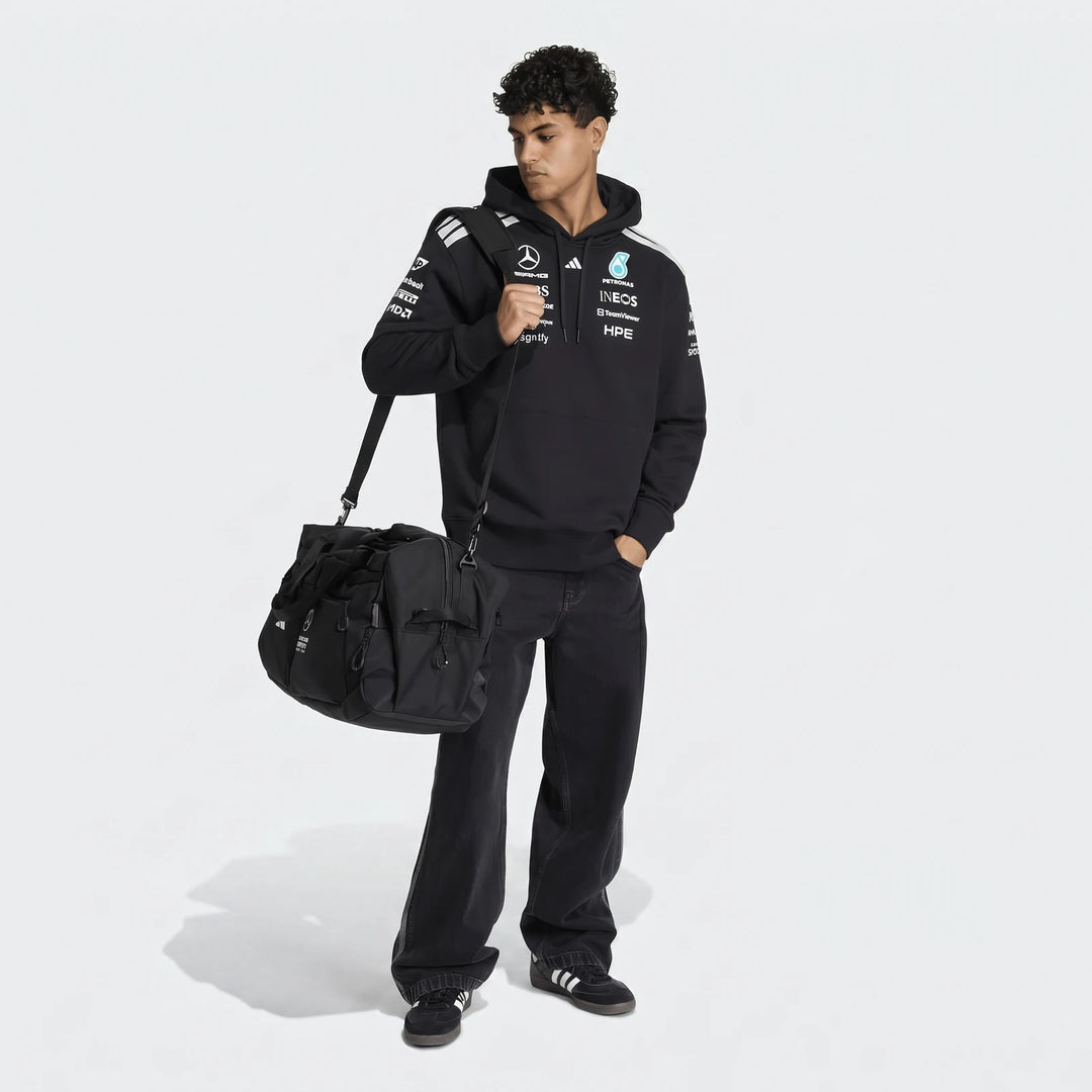 Full body shot of a male model wearing a black Mercedes-AMG Petronas Formula 1 Team Driver Hoodie, black jeans, and