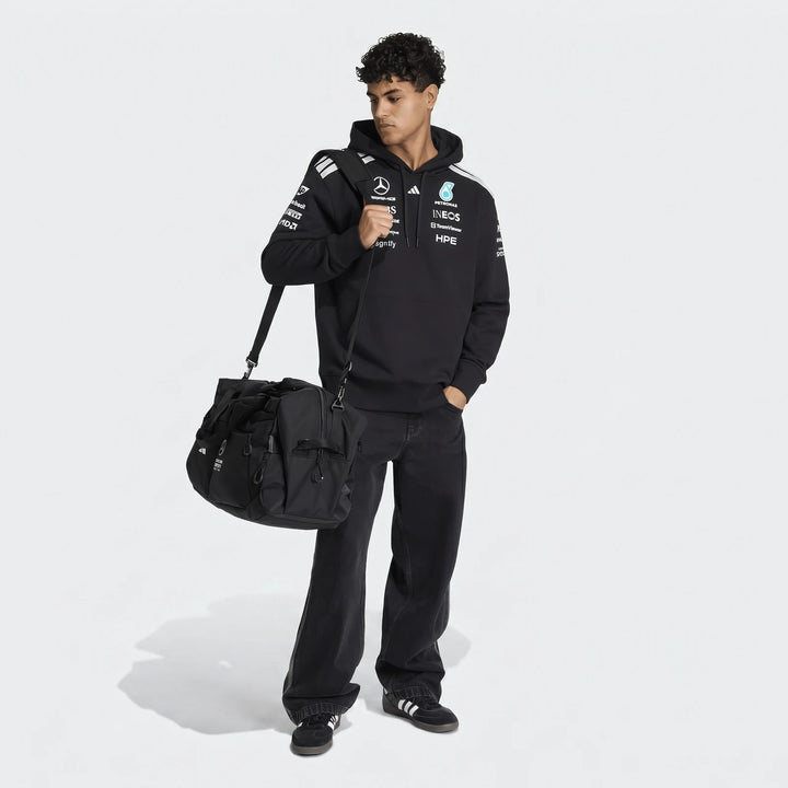Full body shot of a male model wearing a black Mercedes-AMG Petronas Formula 1 Team Driver Hoodie, black jeans, and