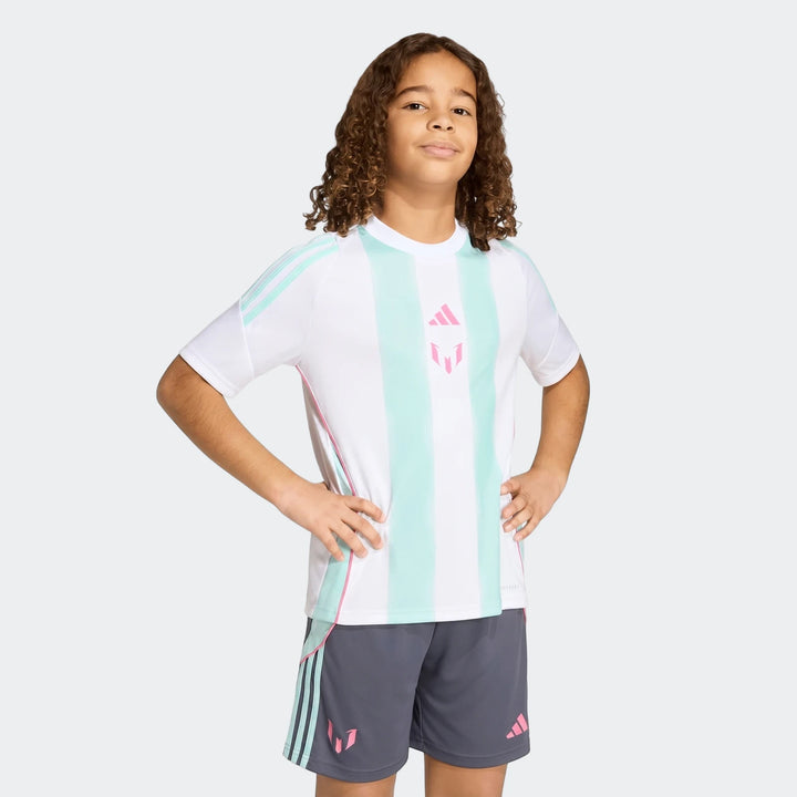 A young boy models the Messi Training Jersey Youth, a white shirt with mint and pink stripes, paired with dark gray shorts.