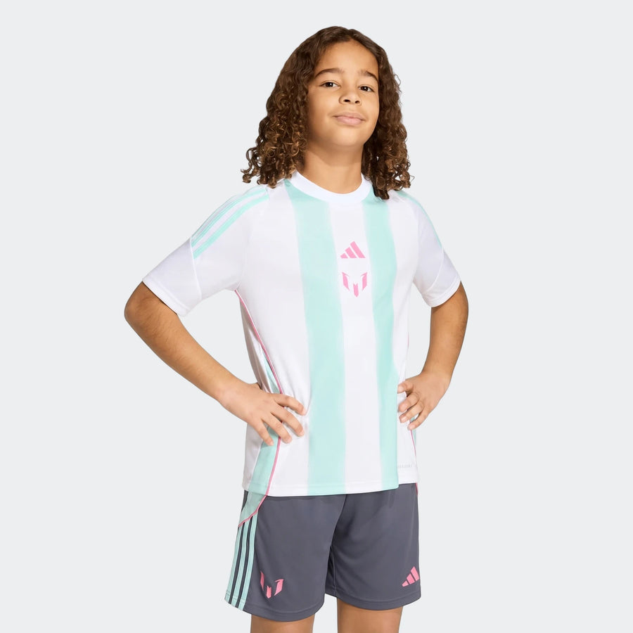 A young boy models the Messi Training Jersey Youth, a white shirt with mint and pink stripes, paired with dark gray shorts.