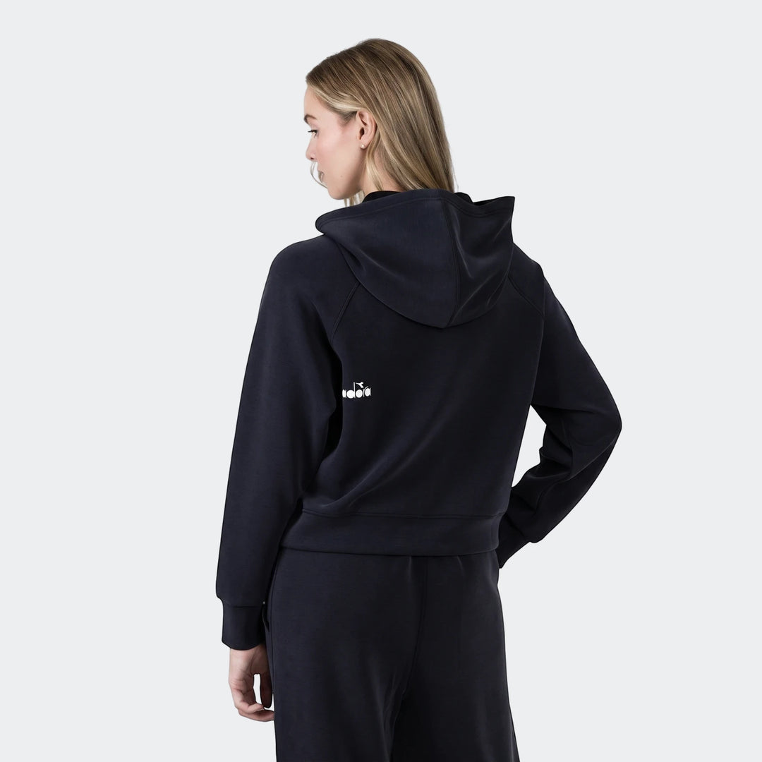 Woman wearing a black Diadora Michelle Hoodie and matching sweatpants, viewed from the back with a slight turn of the head,