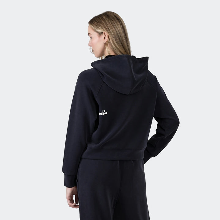 Woman wearing a black Diadora Michelle Hoodie and matching sweatpants, viewed from the back with a slight turn of the head,