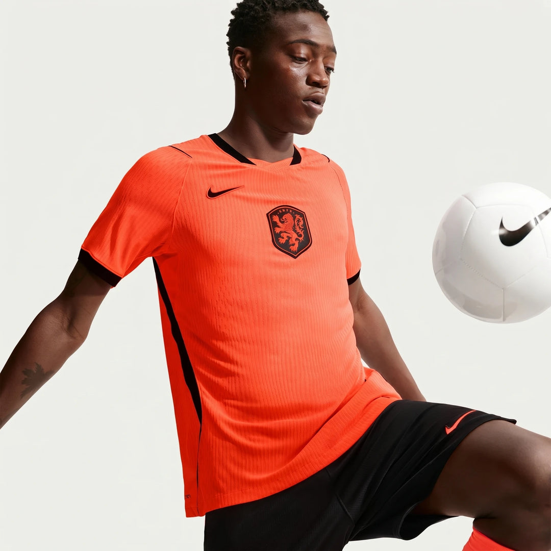 Netherlands National Team 2026 Match Home Orange Men's Nike Aero-Fit Soccer Jersey on a model, dribbling a white Nike soccer