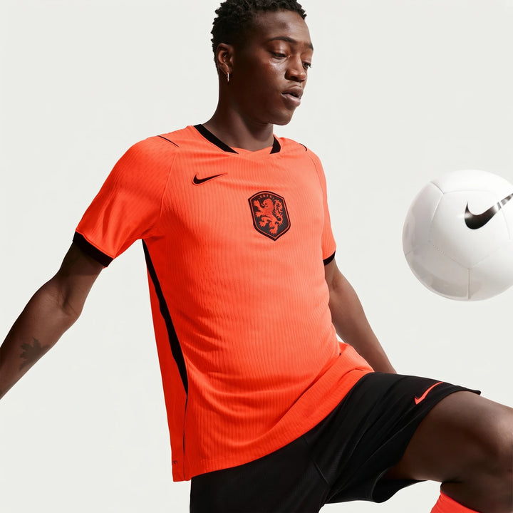 Netherlands National Team 2026 Match Home Orange Men's Nike Aero-Fit Soccer Jersey on a model, dribbling a white Nike soccer